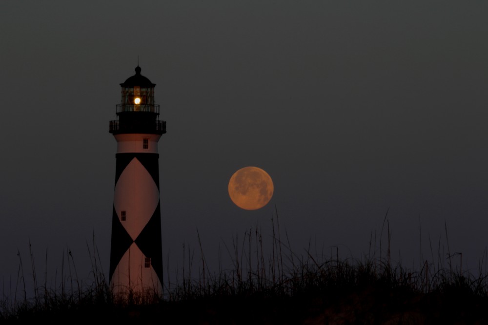 I rose early and hiked down the beach with the moon now setting behind Core banks and on the opposite side of the lighthouse. As the moon slipped closer to the horizon it became tinged with orange as the rising sun applied the color. It soon slipped into the waters of Lookout Bight and the night was over.