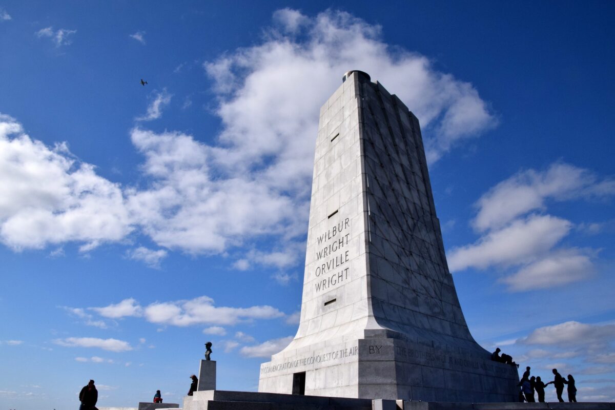 A plane flies over the Wright Brothers Memorial in November 2019. Photo: Jennifer Allen