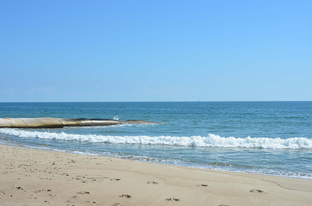 A photo simulation of the view from Bald Head Island looking toward the Wilmington East WEA with 200 wind turbines on the horizon 15 nautical miles offshore on a partly cloudy late afternoon in April. The island's terminal groin is shown at left. Image: BOEM