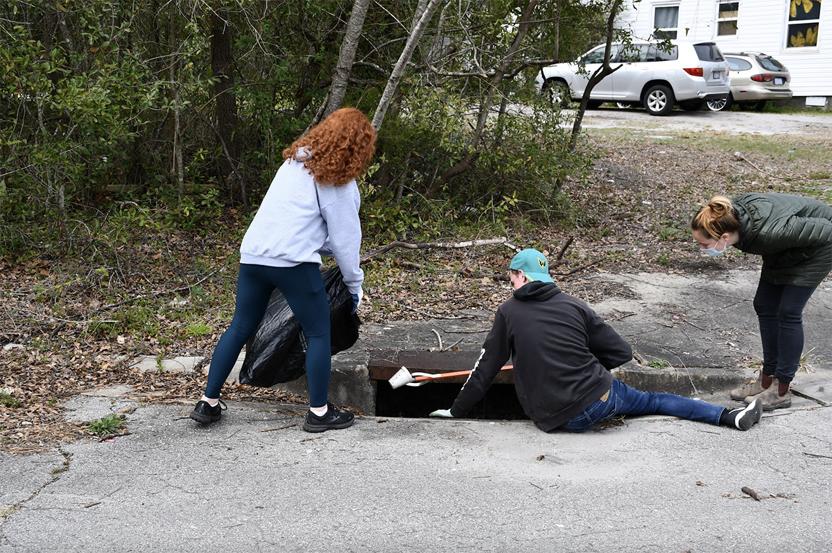 High schoolers volunteering with Cape Fear River Watch pick up trash out of a storm drain to prevent it from getting into waterways. Photo courtesy Cape Fear River Watch 