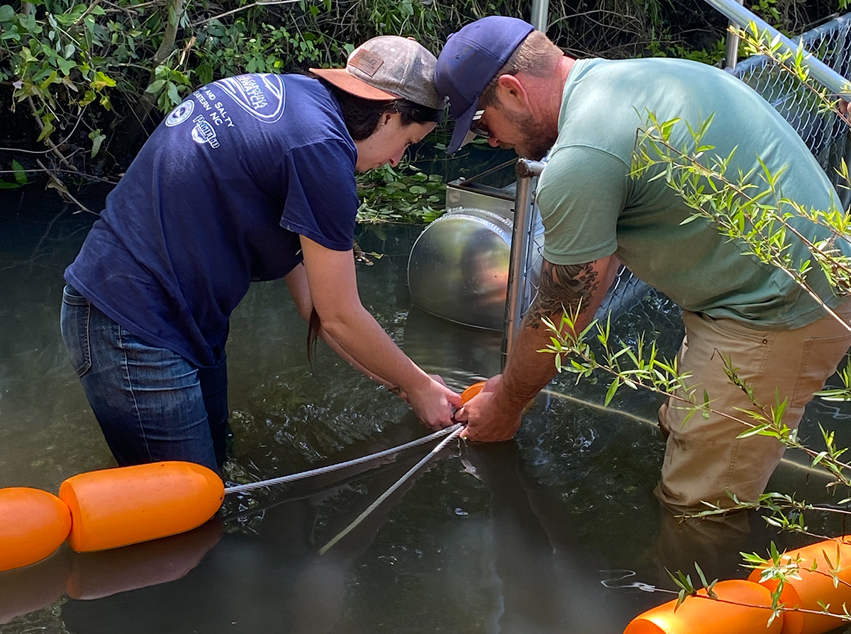 Becca Drohan, White Oak Waterkeeper, left, and Aaron Houran, water quality technician for Jacksonville’s stormwater department, install a Trash Trout litter trap in a tributary of the New River. Photo: Contributed