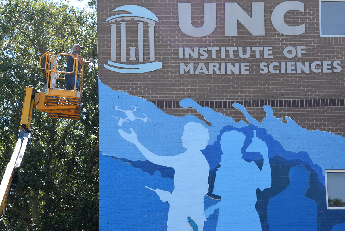 Matt Dowdle works atop a cherry picker Tuesday on his official mural on the UNC Institute of Marine Sciences façade in Morehead City. Photo: Mark Hibbs 