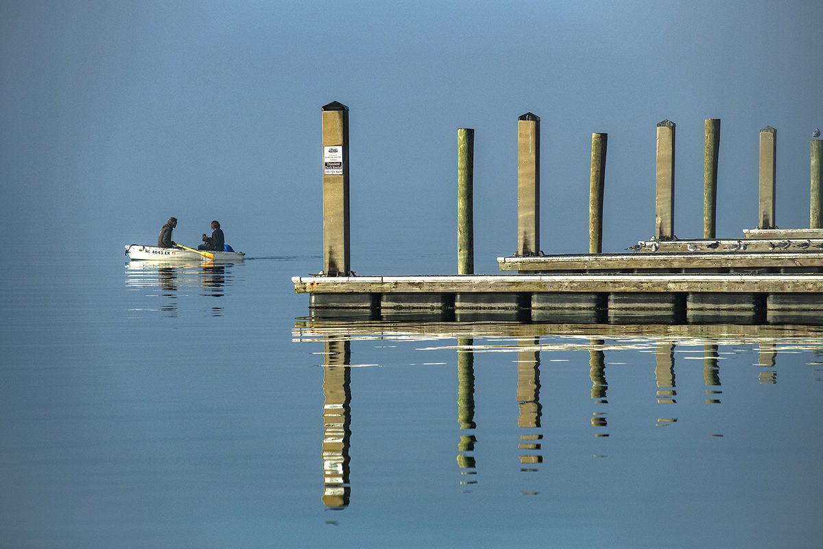 Two unidentified people paddle a dinghy into the cut near Sugarloaf Island from the Morehead City waterfront on a recent foggy morning in Carteret County. Photo: Dylan Ray