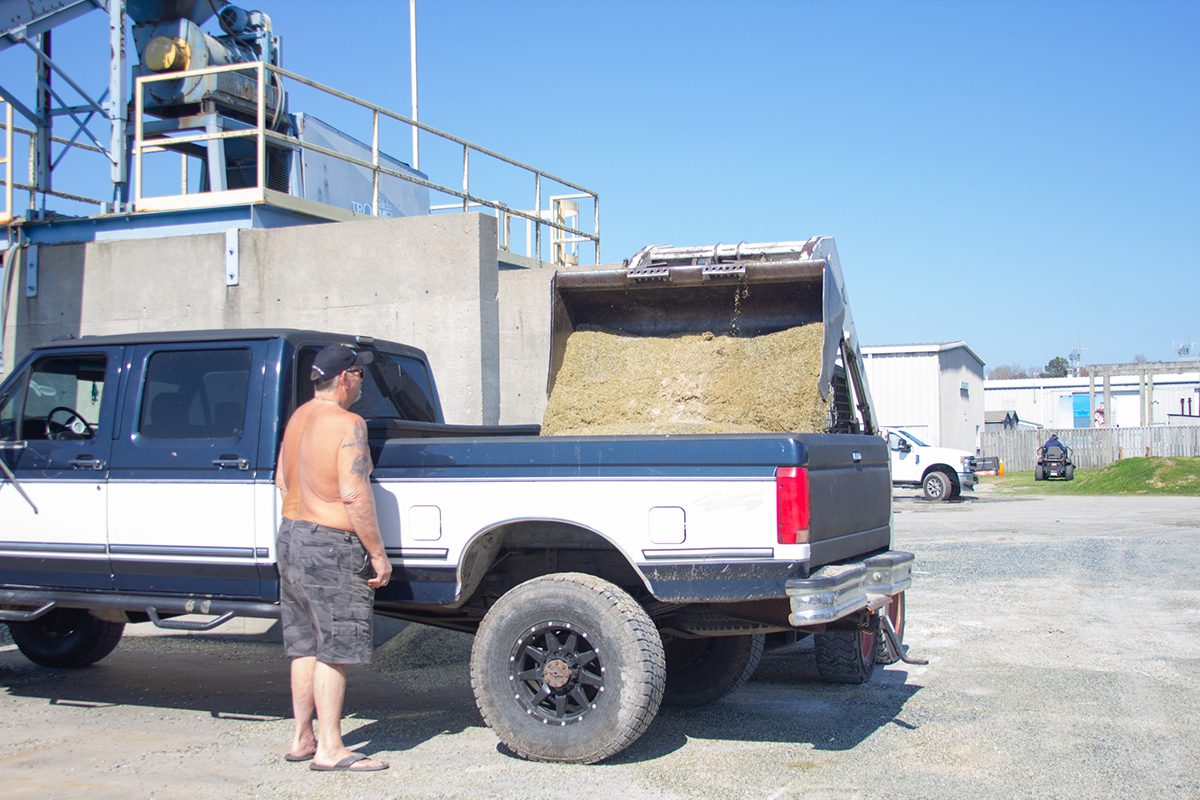 A Roanoke Island man watches as a Dare County Public Works employee loads sand made from crushed glass bottles into his truck. Photo: Corinne Saunders