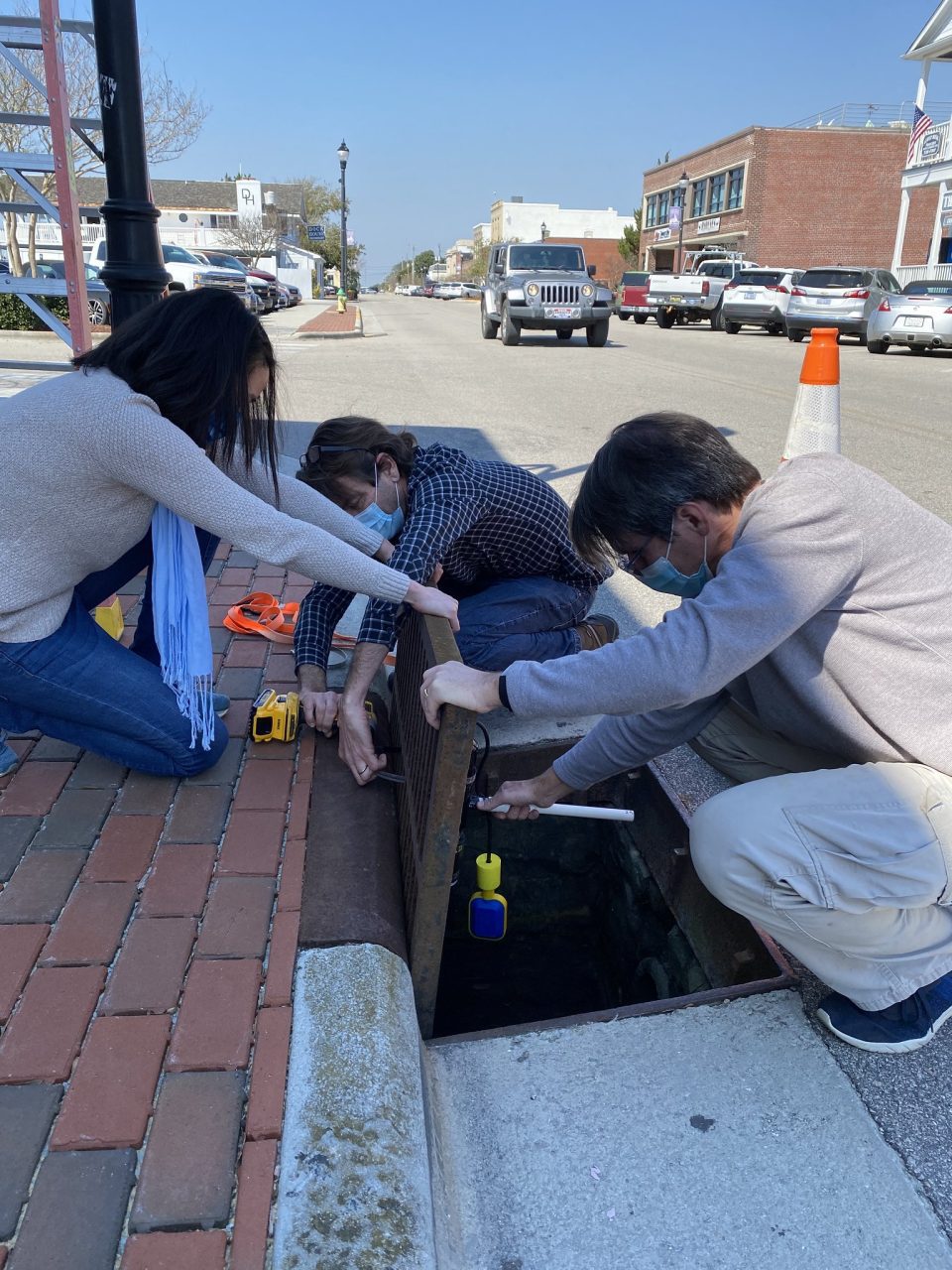 Researchers, from left, Dr. Miyuki Hino, Ryan Neve and Tony Whipple deploy a sensor in a Front Street storm drain in Beaufort in March 2021. Photo: K. Anarde/NCSU
