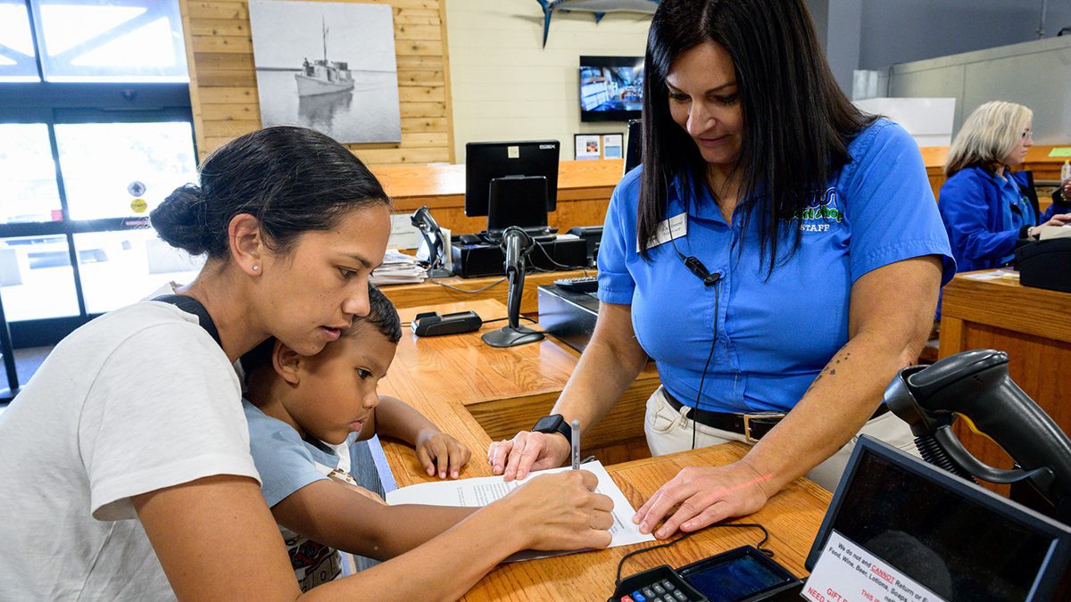 Chelsea and Evan Kekahuna. left, of Stella, sign for his lifetime license with assistance from LaVonne Lampasona, a supervisor at Neuse Sports Shop in Cedar Point. Photo: NCDMF