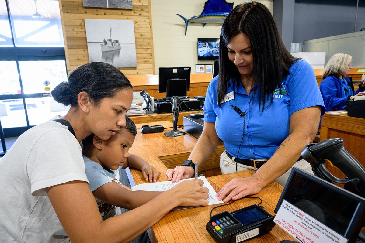 Chelsea and Evan Kekahuna, left, of Stella sign for his lifetime license with assistance from LaVonne Lampasona, a supervisor at Neuse Sports Shop in Cedar Point. Photo: NCDMF