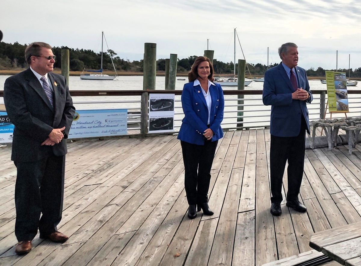 Sen. Norm Sanderson, R-Pamlico, who also represents Carteret County, right, addresses Wednesday a small crowd in downtown Morehead City to celebrate the start of the Sugarloaf Island restoration project as Mayor Jerry Jones, left, and Rep. Celeste C. Cairns, R-Carteret and Craven counties, look on. Photo: Jennifer Allen