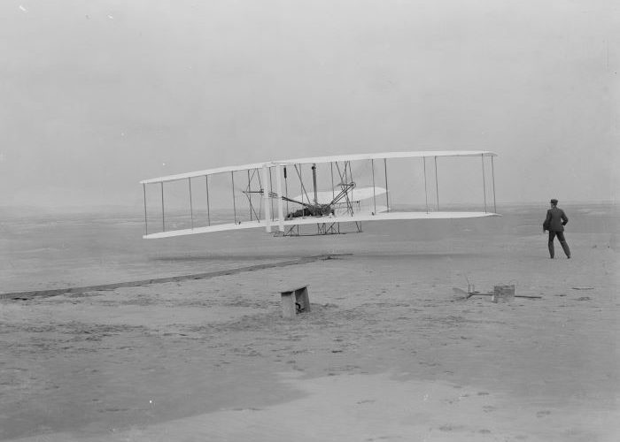 Orville Wright takes off in the first flight of the 1903 flyer as Wilbur Wright assists. Photo: NPS