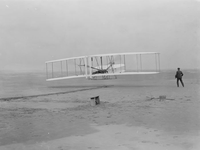 Orville Wright takes off in the first flight of the 1903 flyer as Wilbur Wright assists. Photo: NPS
