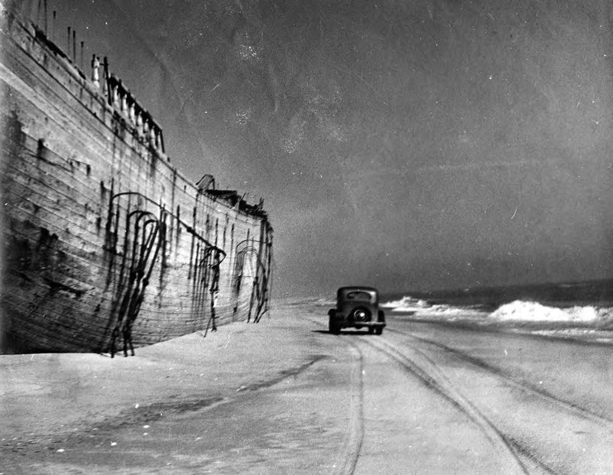 Driving down Outer Banks beach by shipwreck. Photo: D. Victor Meekins Papers, Outer Banks History Center
