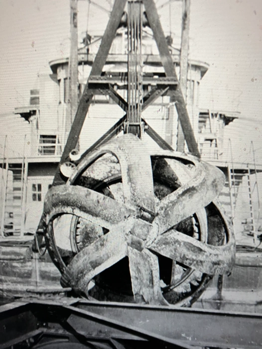 This intimidating bit of machinery is a cutterhead (a.k.a. “rotary cutter”) resting on the deck of the Currituck in 1932. As you can see, this is a very different beast than the kind of dredge that we saw being used on derrick barge No. 14. Attached to the inlet end of a hydraulic dredge’s suction pipe, this cutterhead was a powerful, rotating instrument that broke up and then sucked in sand, mud, rock, and pretty much everything else at a dredging site, including the sea life. The dredge’s centrifugal pumps carried the loose material into pipes, which in turn carried the material to a dump site– either a barge for transport elsewhere or to a dredge spoil island or shoreline nearby. This photograph comes from the W. W. Old Collection at the Mariners Museum, Newport News, Va.
