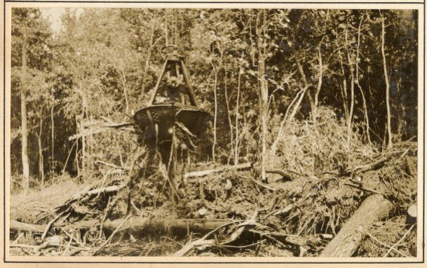 Here we can see derrick barge No. 14’s orange-peel bucket cutting off a point of land that was protruding into the Scuppernong River, May 1931. An “orange-peel bucket” is a kind of bucket dredge, of which there are two kinds. A “clam-shell” bucket has two jaws (or shells), while the “orange-peel bucket” that we see here has three or four jaws. Both kinds of bucket dredge work the same way. The bucket hangs from a pair of wires or chains hung from the end of the dredge’s boom and powered by a double cylinder, double drum steam engine. On No. 14, the hoist operator used those wires to lower the bucket, open the bucket’s jaws and draw in earth and vegetation. He then closed and raised the bucket, turned the boom, and either lowered the load onto a scow or, in this case, onto the banks of the Scuppernong. Source: Office of History, HQ, U.S. Army Corps of Engineers
