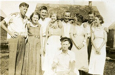 Troy Elliott (standing 5th from left) at an ice cream social with a crowd of local friends in Hyde County, 1935. The back of the photograph identifies the group as (standing left to right): Edward Gibbs, Hilda Midgett, Audrey Cahoon, Sybil Midgett, Troy Elliott, Eva Gray Berry, Belton Midgett, and an unidentified young woman, with Cecil Gibbs kneeling with the ice cream maker. The young men may have been among the Hyde County enrollees who served with Troy Elliott at Bell Island. Photo courtesy, State Archives of North Carolina
