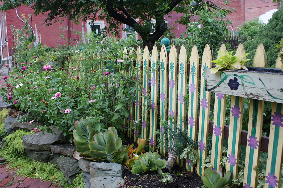 In this streetside garden, a raised bed constructed of stacked stone creates space for growing zinnias and other plants between the sidewalk and a charming painted picket fence. Photo: Barbara W. Ellis