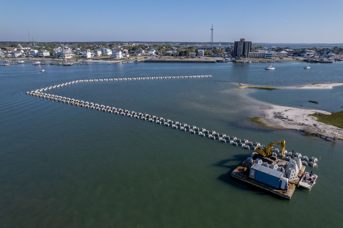 This late-April aerial view includes wave attenuators being placed around the west side of Sugarloaf Island, with downtown Morehead City in the background, part of a hybrid project to restore the eroding barrier island. Photo: Dylan Ray