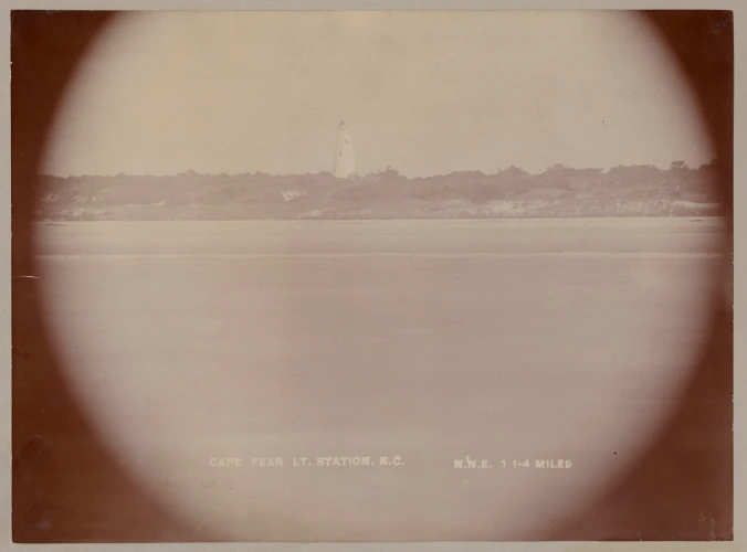 Telescopic view of the Bald Head Light Station from the waters off Bald Head Island, November 1896. Originally built in 1817, the lighthouse was long a welcome sight to mariners at the entrance to the Cape Fear River. In July 1834, Capt. Henry D. Hunter of the revenue cutter Tanker described the Light as having 15 lamps, being 109 feet above the level of the sea, and showing a fixed light. On an inspection tour two years later, he reported, “The keeper is an old Revolutionary [War] soldier and is unable from sickness to give the lighthouse his constant personal attention. The light, however, shows well from a distance.” Source of quote: U.S. Coast Guard Historian’s Office.  Source of Photograph: Records of the U.S. Coast Guard (RG 26), National Archives-College Park

