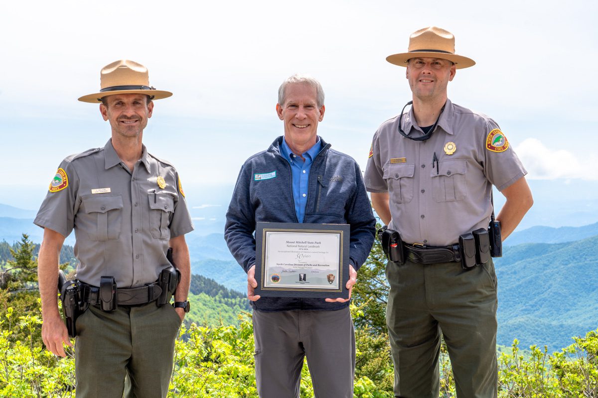 West District Superintendent Sean McElhone, left, Department of Natural and Cultural Resources Secretary Reid Wilson and Mount Mitchell Superintendent Robert McGraw commemorate Mount Mitchell’s 50th anniversary as a National Natural Landmark. Photo: N.C. State Parks