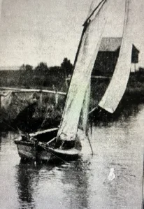 A sail skiff on Mashoes Creek, with net reels and a fish camp built on pilings in the background, 1939. Greensboro News & Record (19 Nov. 1939)