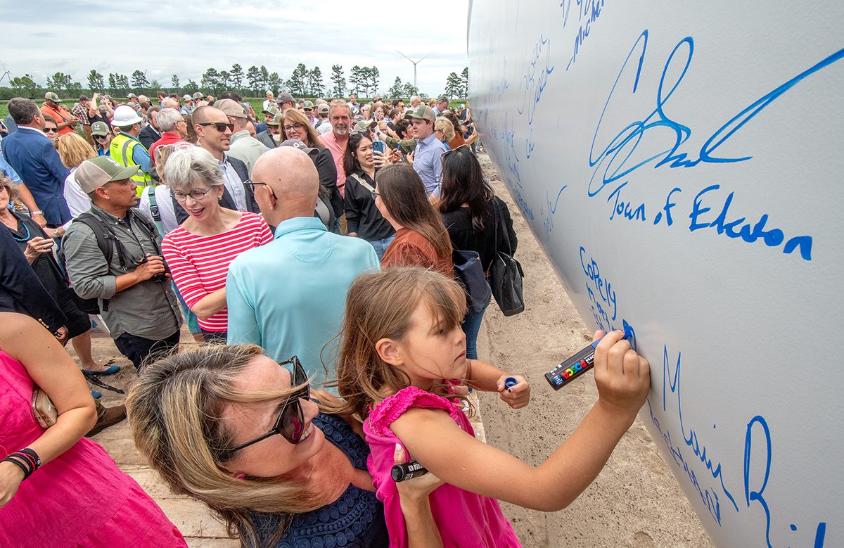 Copely Morton-Estes, right, is lifted up by her mother Rachel Estes as she and others from the area add their autographs to a wind turbine blade Wednesday at Timbermill Wind near Edenton. Photo: Dylan Ray