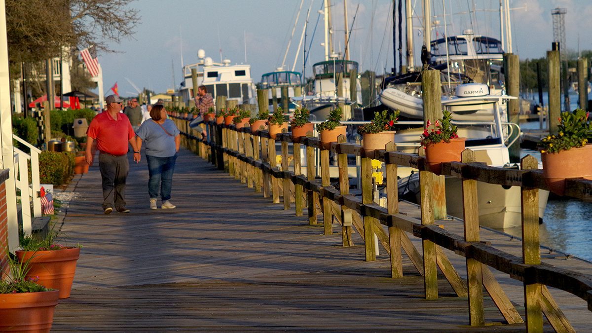 Couples stroll the Beaufort waterfront boardwalk in April, glancing toward the docks on Taylors Creek and the Rachel Carson Reserve just beyond. Photo: Mark Hibbs