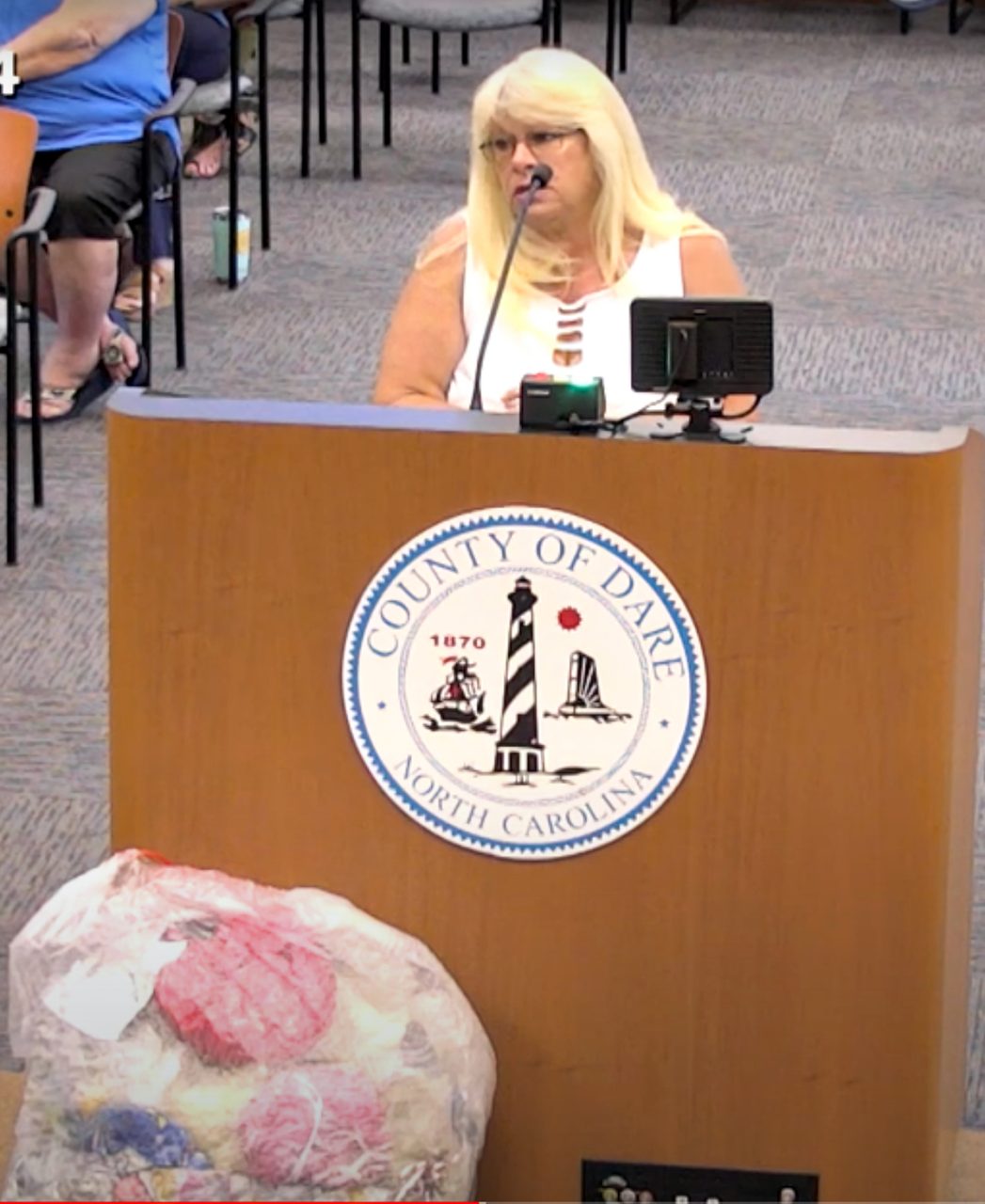 Debbie Swick speaks during a recent Dare County Board of Commissioners meeting. Also in this screenshot from the meeting video, a bag of balloons she found on the beach rests on the floor next to the podium.
