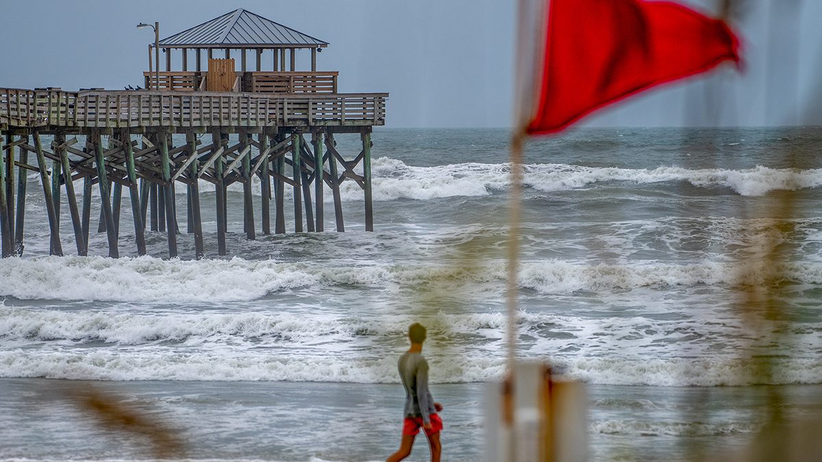 A beachgoer passes by a red flag as Tropical Storm Debby pushes storm swell against the Oceanana Pier Wednesday in Atlantic Beach along Bogue Banks. Photo: Dylan Ray