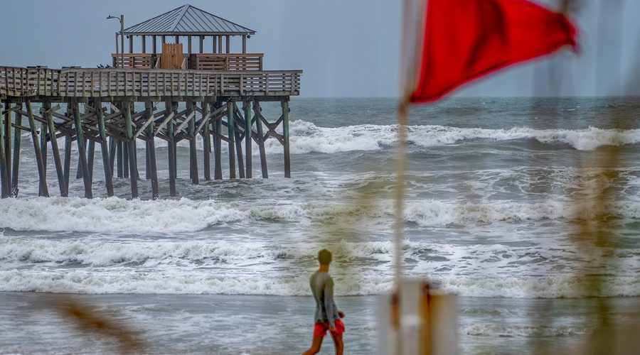 A beachgoer passes by a red flag as Tropical Storm Debby pushes storm swell against the Oceanana Pier Wednesday in Atlantic Beach along Bogue Banks. Photo: Dylan Ray