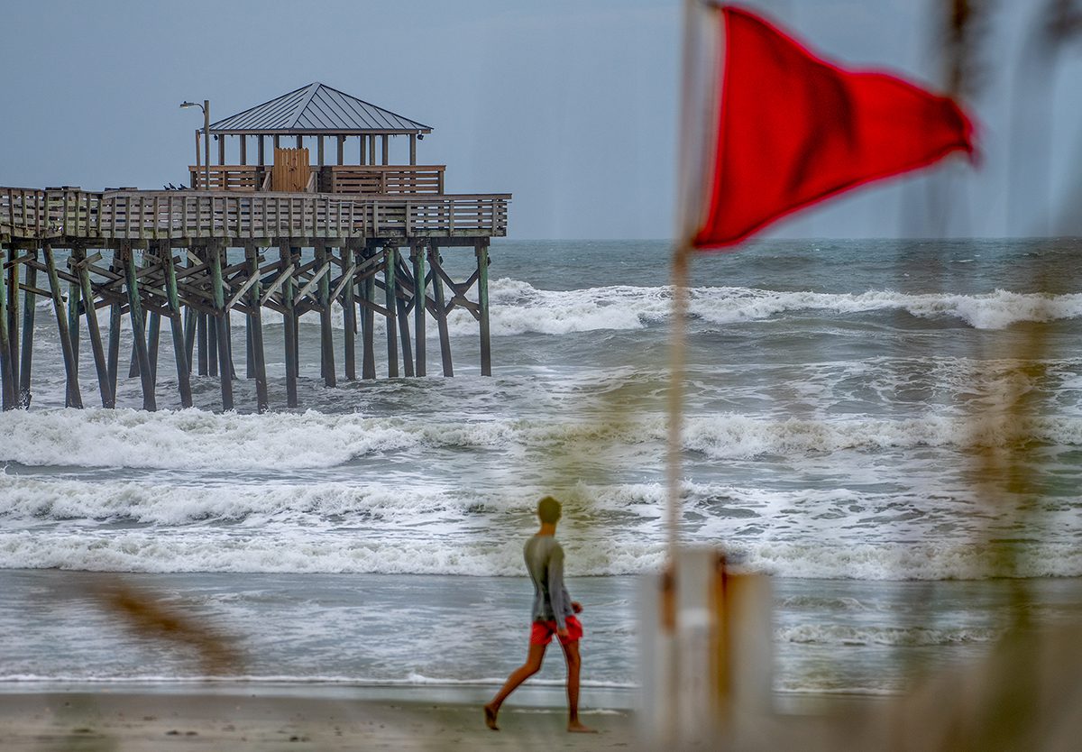 A beachgoer passes by a red flag as Tropical Storm Debby pushes storm swell against the Oceanana Pier Wednesday in Atlantic Beach along Bogue Banks. Photo: Dylan Ray