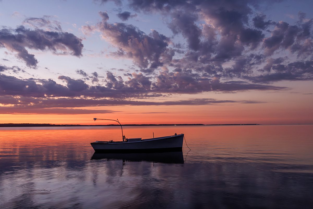 A fishing skiff anchored at the North River Bridge in Otway, in Carteret County, is nearly silhouetted at dawn recently. Photo: Doug Waters