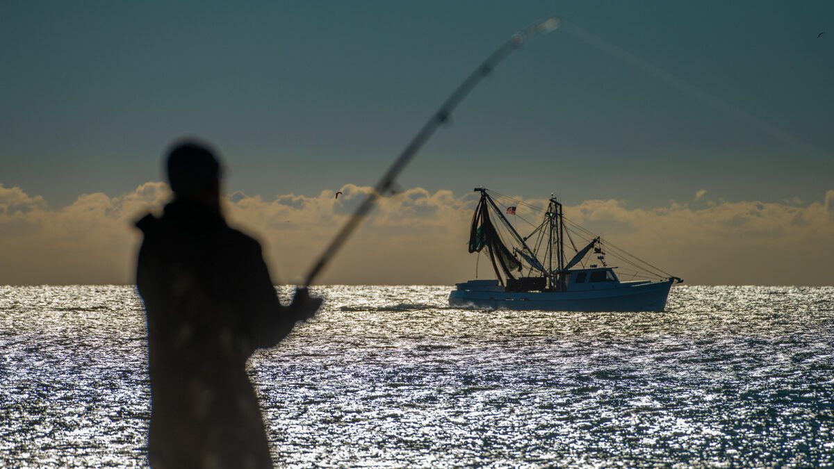 Kevin Hardy of Wilmar, near Vanceboro, fishes along Cape Lookout National Seashore as a commercial fishing trawler offshore heads southwest. Photo: Dylan Ray