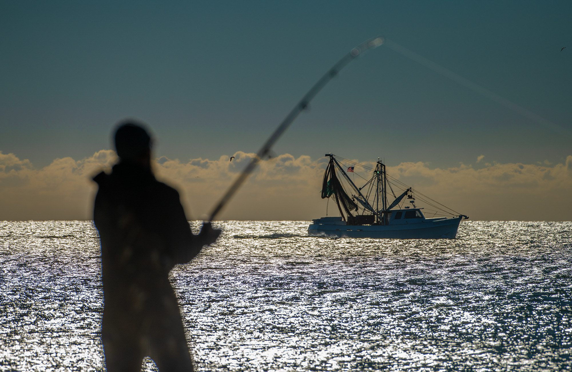 Kevin Hardy of Wilmar, near Vanceboro, fishes along Cape Lookout National Seashore as a commercial fishing trawler offshore heads southwest. Photo: Dylan Ray