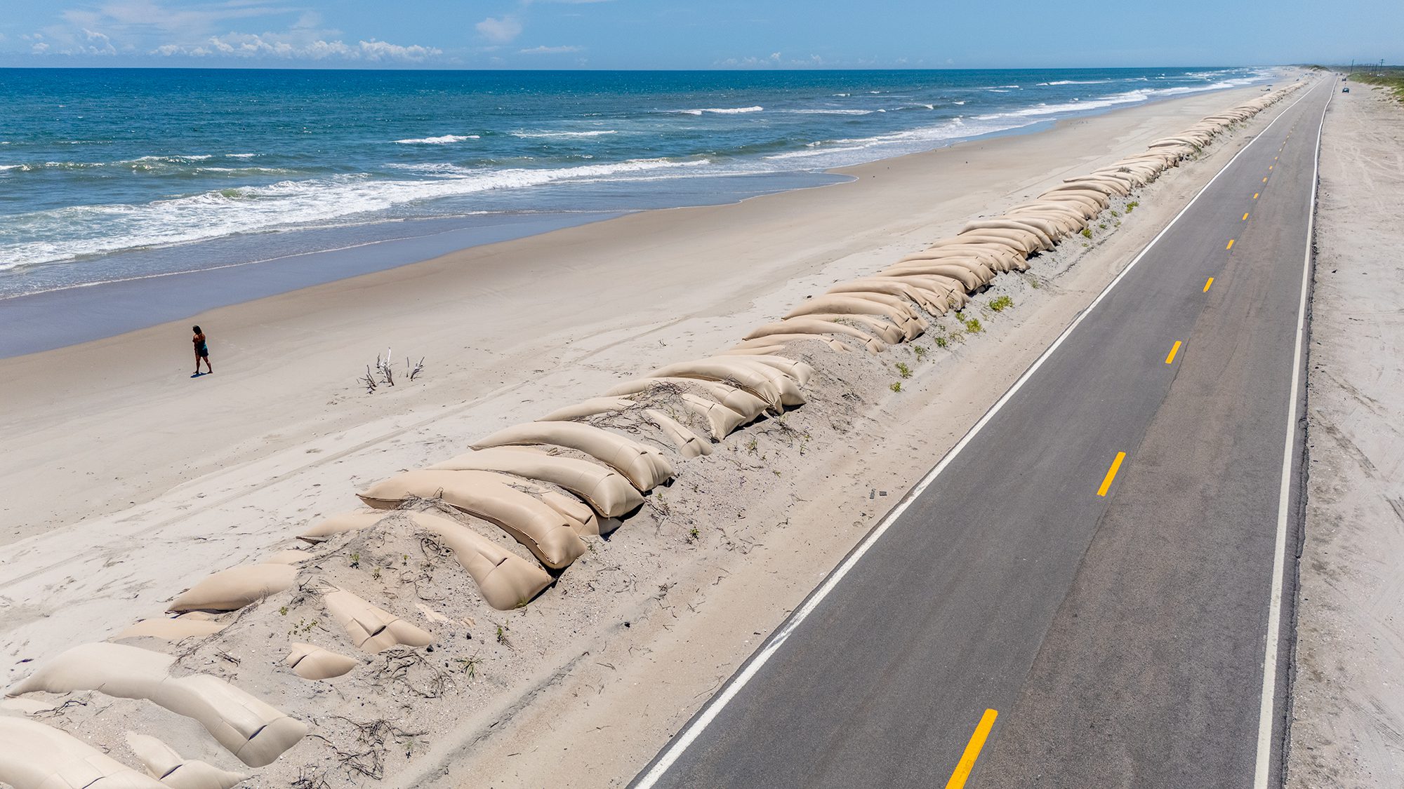 A wall of sandbags extends along the roadside far into the distance aside N.C. Highway 12 on the north end of Ocracoke Island. This is where washouts and erosion from storm surge repeatedly chew away at the barrier island beach and roadway, part of the normal ocean dynamics that humans often try to control. Photo: Dylan Ray
