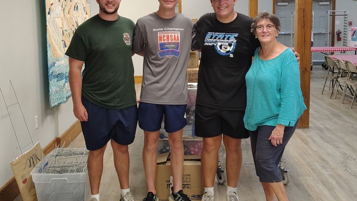 From left, Nick Davies, Jackson Saunders and Liam Calabria, best friends from Raleigh, pose July 3 with Core Sound Waterfowl Museum and Heritage Center Executive Director Karen Amspacher while helping set up for the All American Shrimp Fry that took place July 5. Photo: Jennifer Allen