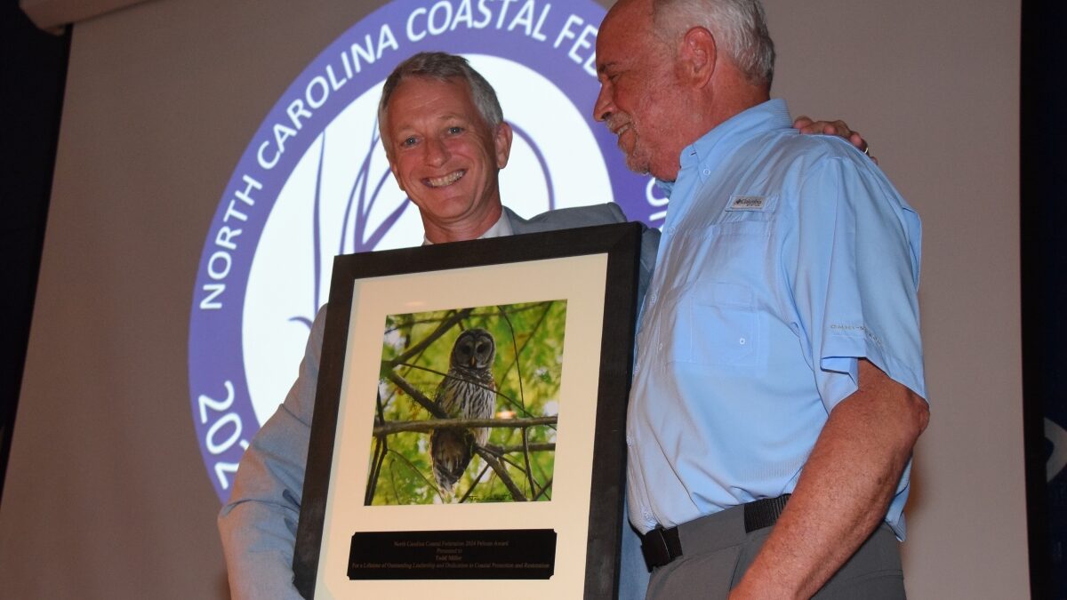 North Carolina Coastal Federation Executive Director Braxton Davis, left, presents an award to the organization's founder and former executive director, Todd Miller, during the 2024 Pelican Awards ceremony in Joslyn Hall on the Carteret Community College campus. Photo: Mark Hibbs
