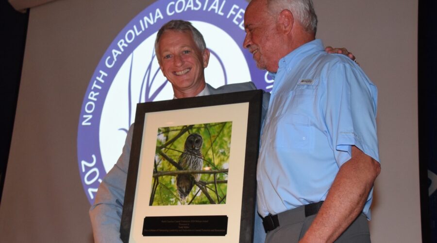 North Carolina Coastal Federation Executive Director Braxton Davis, left, presents an award to the organization's founder and former executive director, Todd Miller, during the 2024 Pelican Awards ceremony in Joslyn Hall on the Carteret Community College campus. Photo: Mark Hibbs