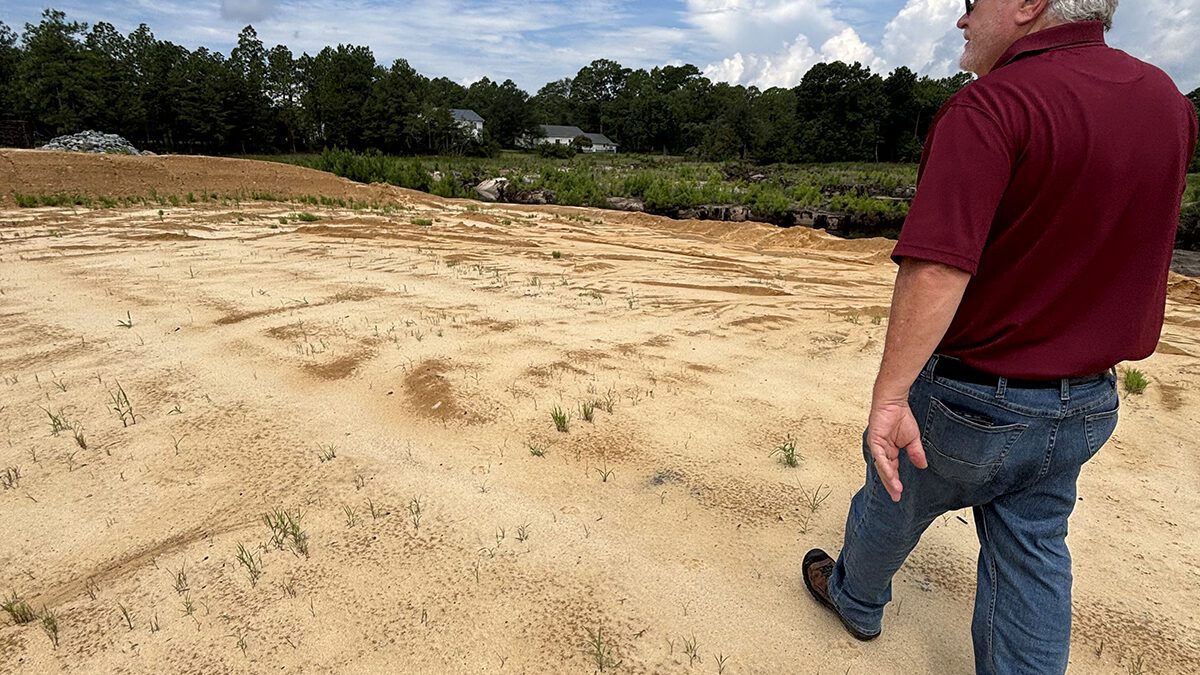 Boiling Spring Lakes Manager David Hargrove on July 30 walks atop Pine Lake Dam where a crucial, unfinished section of one of the city's main routes remains closed. Photo: Trista Talton