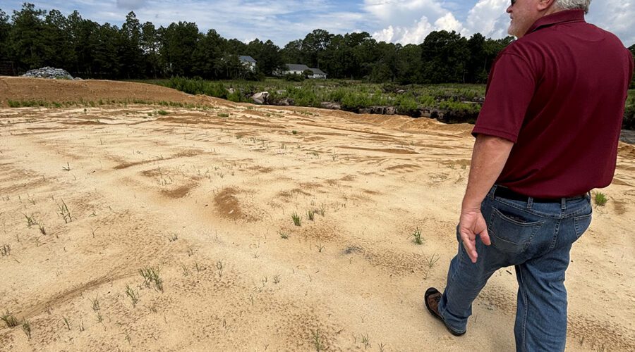 Boiling Spring Lakes Manager David Hargrove on July 30 walks atop Pine Lake Dam where a crucial, unfinished section of one of the city's main routes remains closed. Photo: Trista Talton