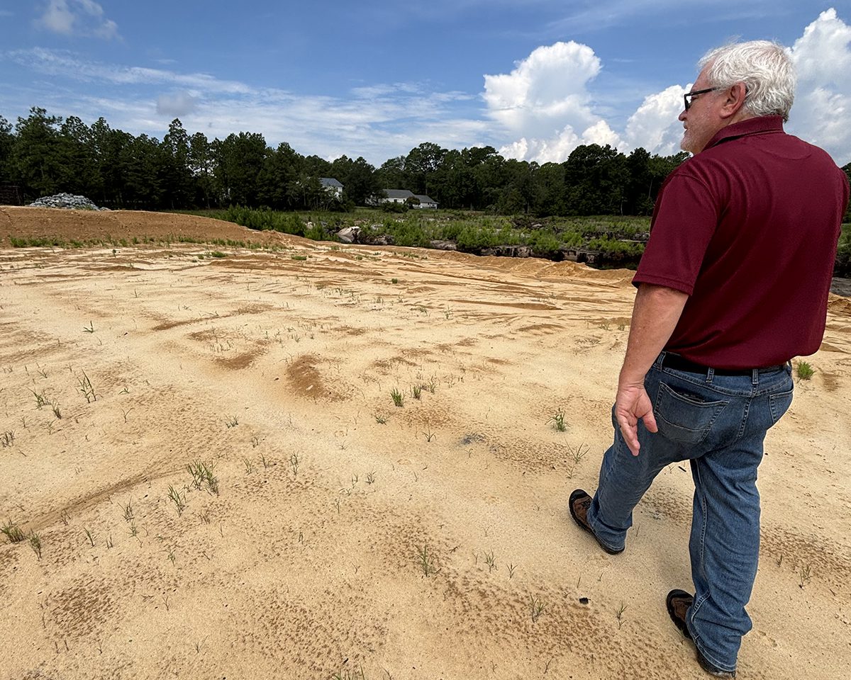 Boiling Spring Lakes Manager David Hargrove on July 30 walks atop Pine Lake Dam where a crucial, unfinished section of one of the city's main routes remains closed. Photo: Trista Talton