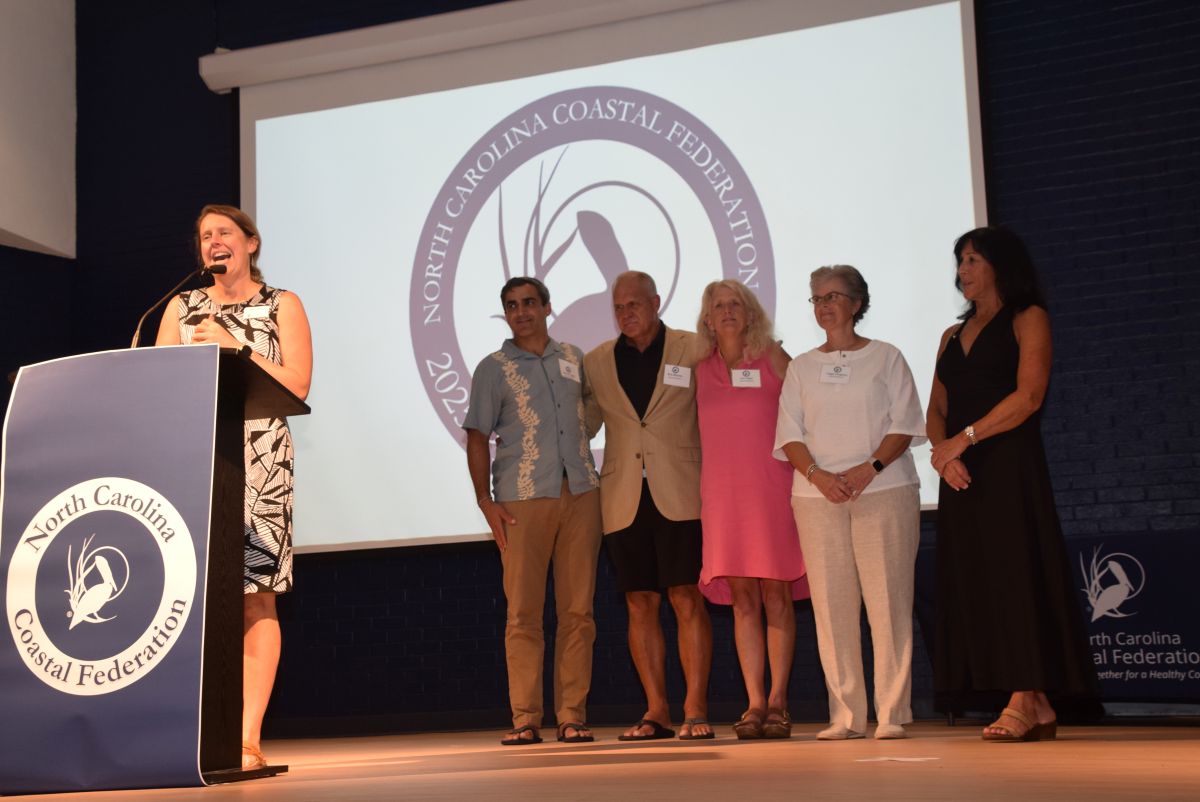 The Coastal Federation's Kerri Allen, a member of the Wrightsville Beach Outrigger Canoe Club, accepts a Pelican Award on behalf of the team, shown in the background. Photo: Mark Hibbs