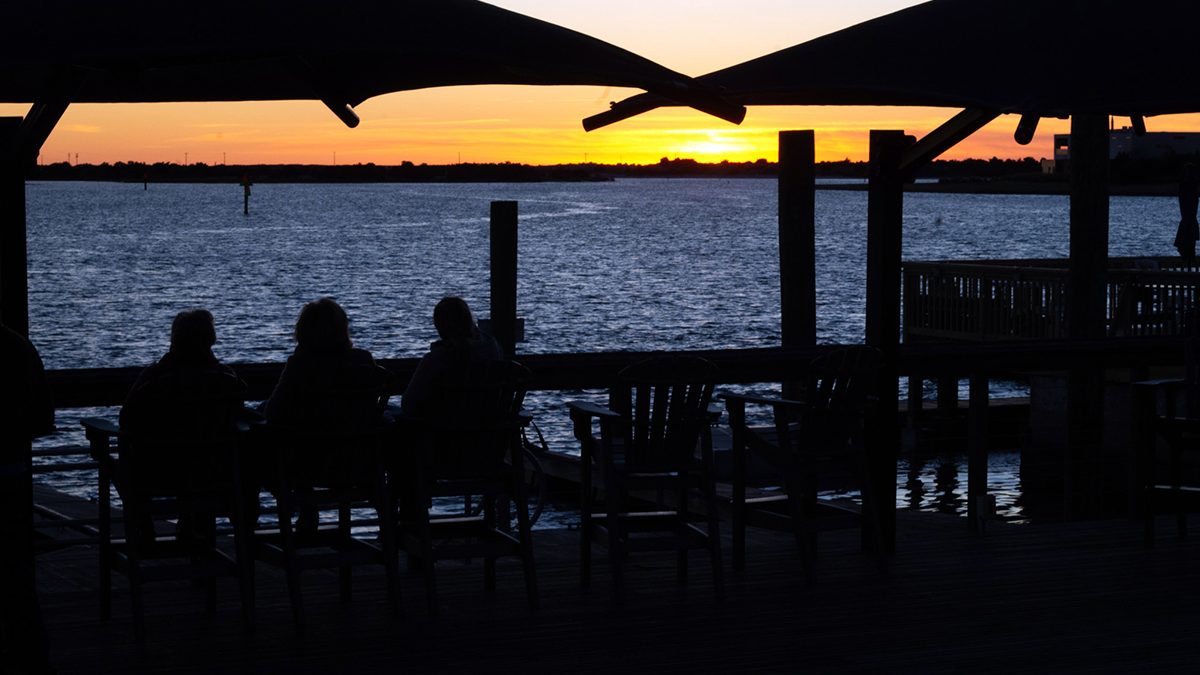 A small gathering watches 2025's final sunset over Taylors Creek from the wooden deck at Harborside Park at 322 Front St. in Beaufort. Photo: Mark Hibbs