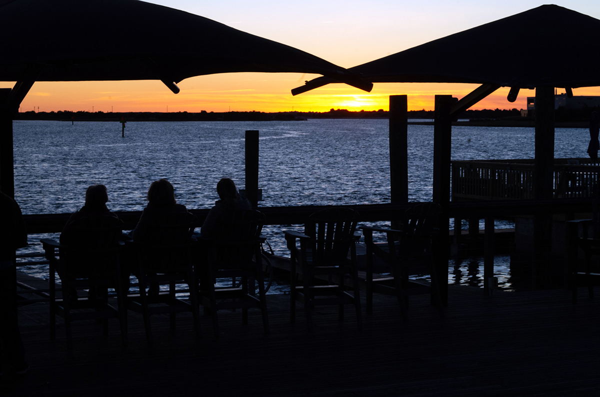 A small gathering watches 2025's final sunset over Taylors Creek from the wooden deck at Harborside Park at 322 Front St. in Beaufort. Photo: Mark Hibbs