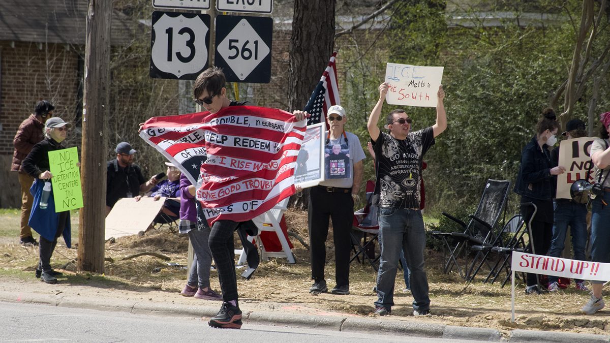 Melissa Stewart carries her flag of protest across the street Saturday in Ahoskie where as many as 40 demonstrated against plans for Immigration and Customs Enforcement to reopen the Rivers Correctional Facility in nearby Winton as a federal immigrant detention center. Photo: Kip Tabb