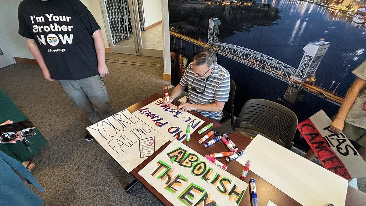 Residents set up at an entrance to the Skyline Center in downtown Wilmington to hand out handmade signs at the Environmental Management Commission's public hearing Thursday on proposed PFAS monitoring and minimization rules. Photo: Trista Talton