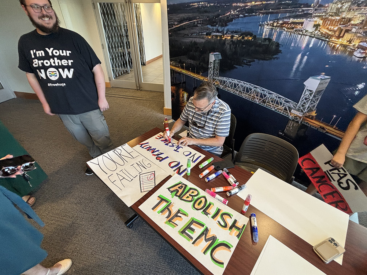 Residents set up at an entrance to the Skyline Center in downtown Wilmington to hand out handmade signs at the Environmental Management Commission's public hearing Thursday on proposed PFAS monitoring and minimization rules. Photo: Trista Talton
