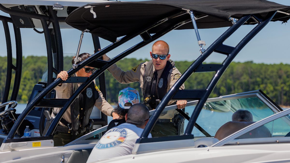 Officers Hannah Shively and Jake Thompson of the N.C. Wildlife Resources Commission Law Enforcement Division talk with boaters on Jordan Lake Tuesday, July 2, 2024. Photo: NCWRC