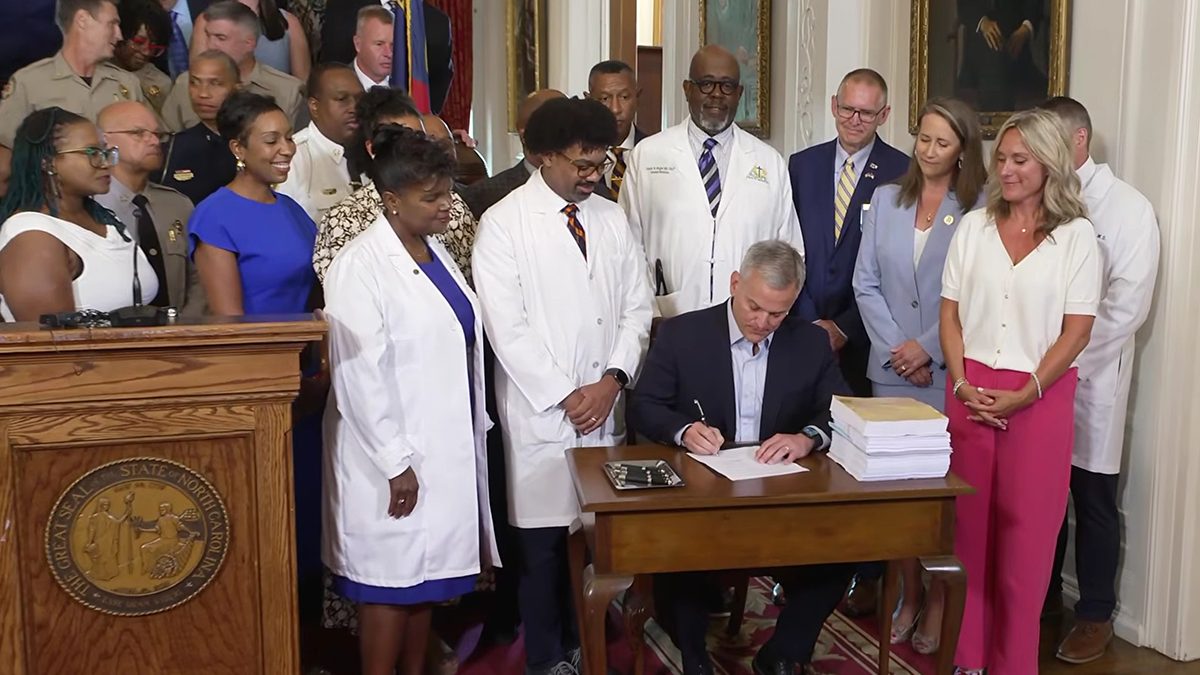 Gov. Josh Stein, surrounded Tuesday by educators, health care providers and public safety officers, signs Senate Bill 257, the 2026 Appropriations Act, in this screenshot from the governor's YouTube channel.