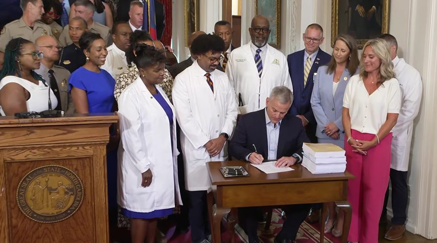 Gov. Josh Stein, surrounded Tuesday by educators, health care providers and public safety officers, signs Senate Bill 257, the 2026 Appropriations Act, in this screenshot from the governor's YouTube channel.