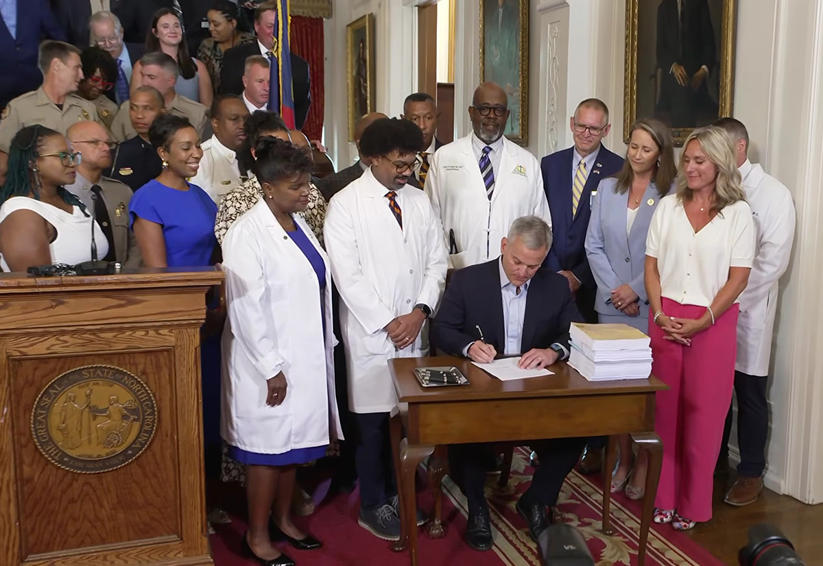 Gov. Josh Stein, surrounded Tuesday by educators, health care providers and public safety officers, signs Senate Bill 257, the 2026 Appropriations Act, in this screenshot from the governor's YouTube channel.