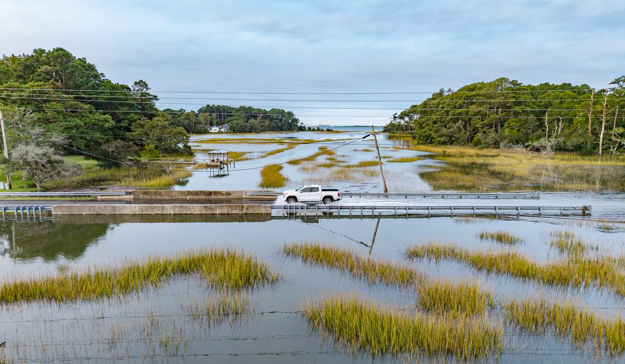 A motorist slows to pass through the high-tide waters on the roadway over Russell Creek Friday near Beaufort. Photo: Dylan Ray